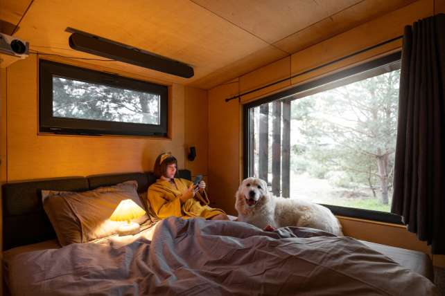 Woman with dog in tiny bedroom of a wooden house on nature