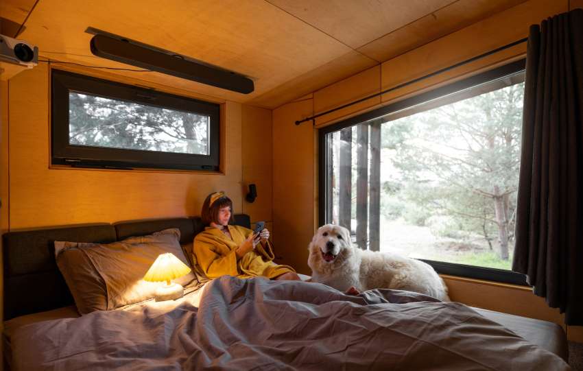 Woman with dog in tiny bedroom of a wooden house on nature